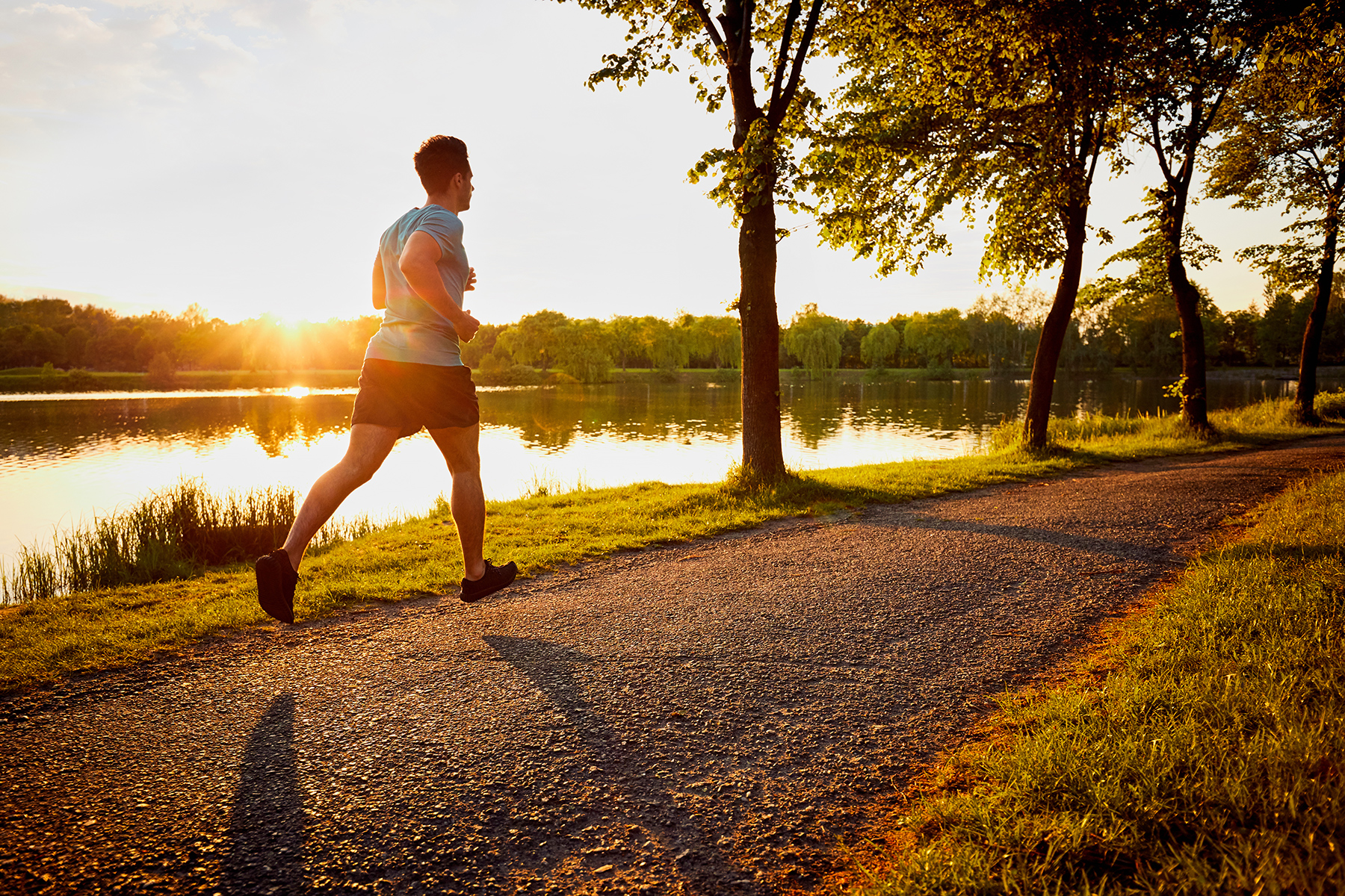 Man jogging along lake trail at sunrise