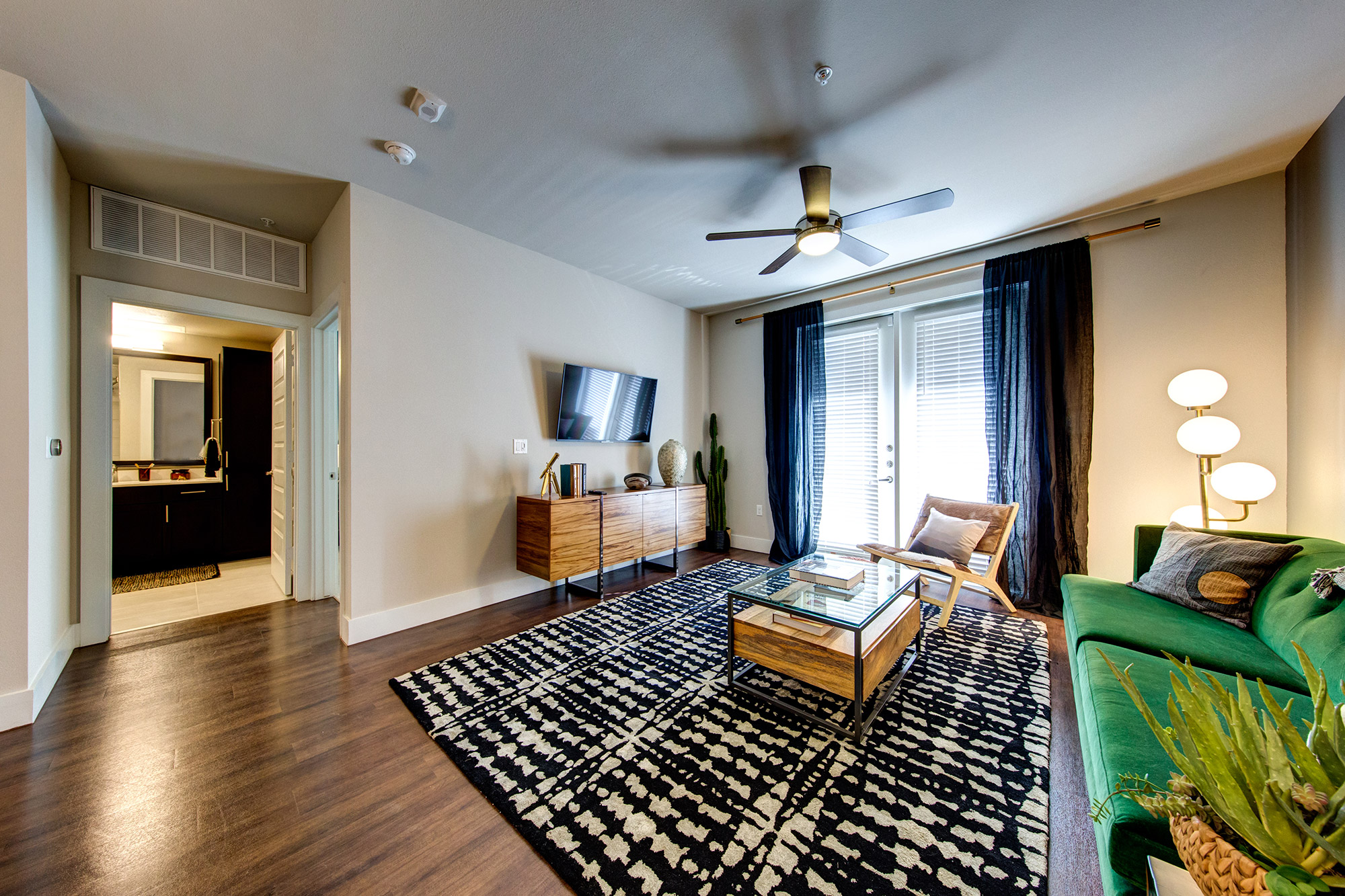 Living room with wood-style flooring, door leading to patio, ceiling fan and modern furniture with access to the bathroom.