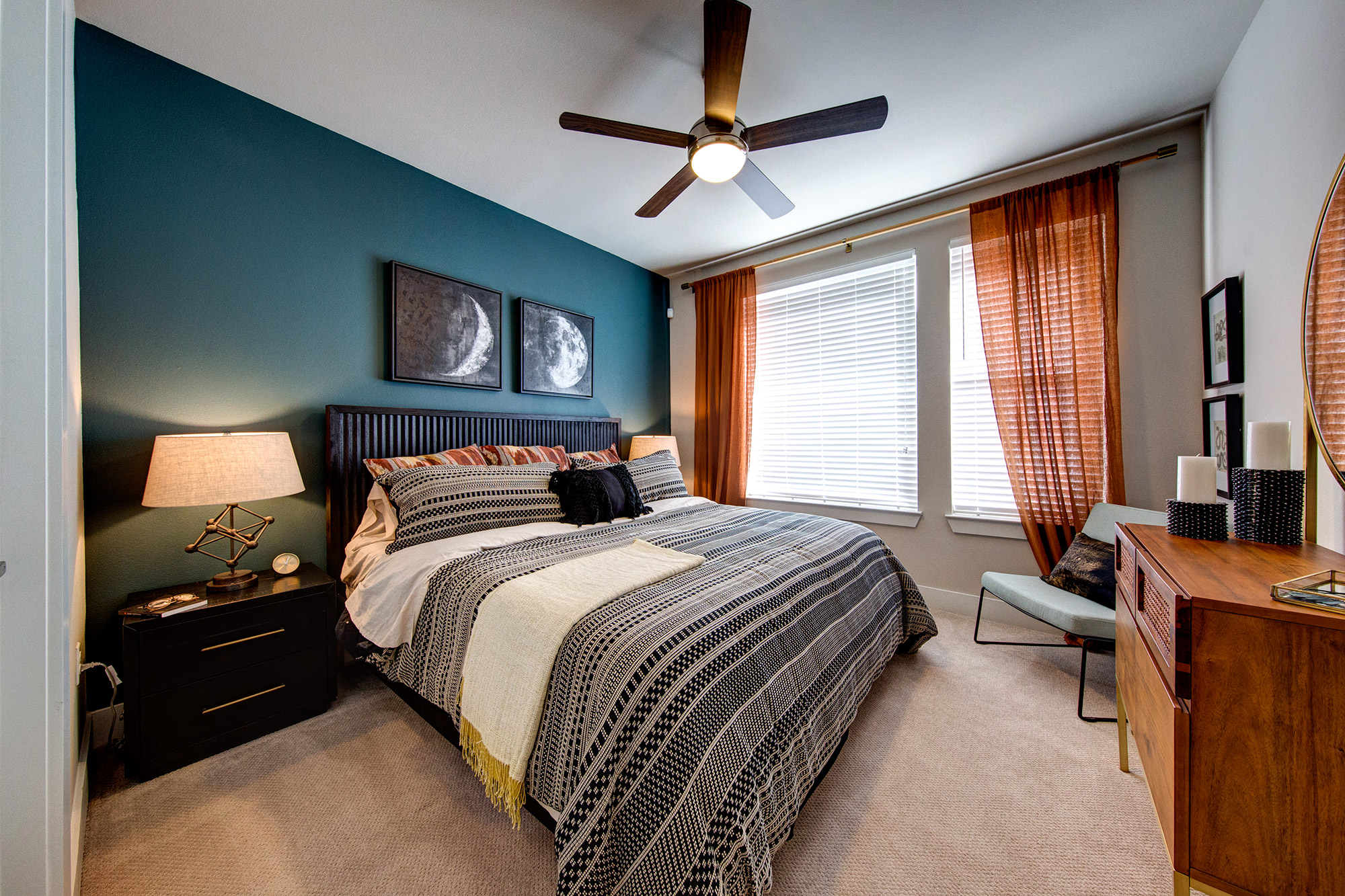 Bedroom with large windows, plush carpeting, ceiling fan, accent wall and modern bedroom furniture.
