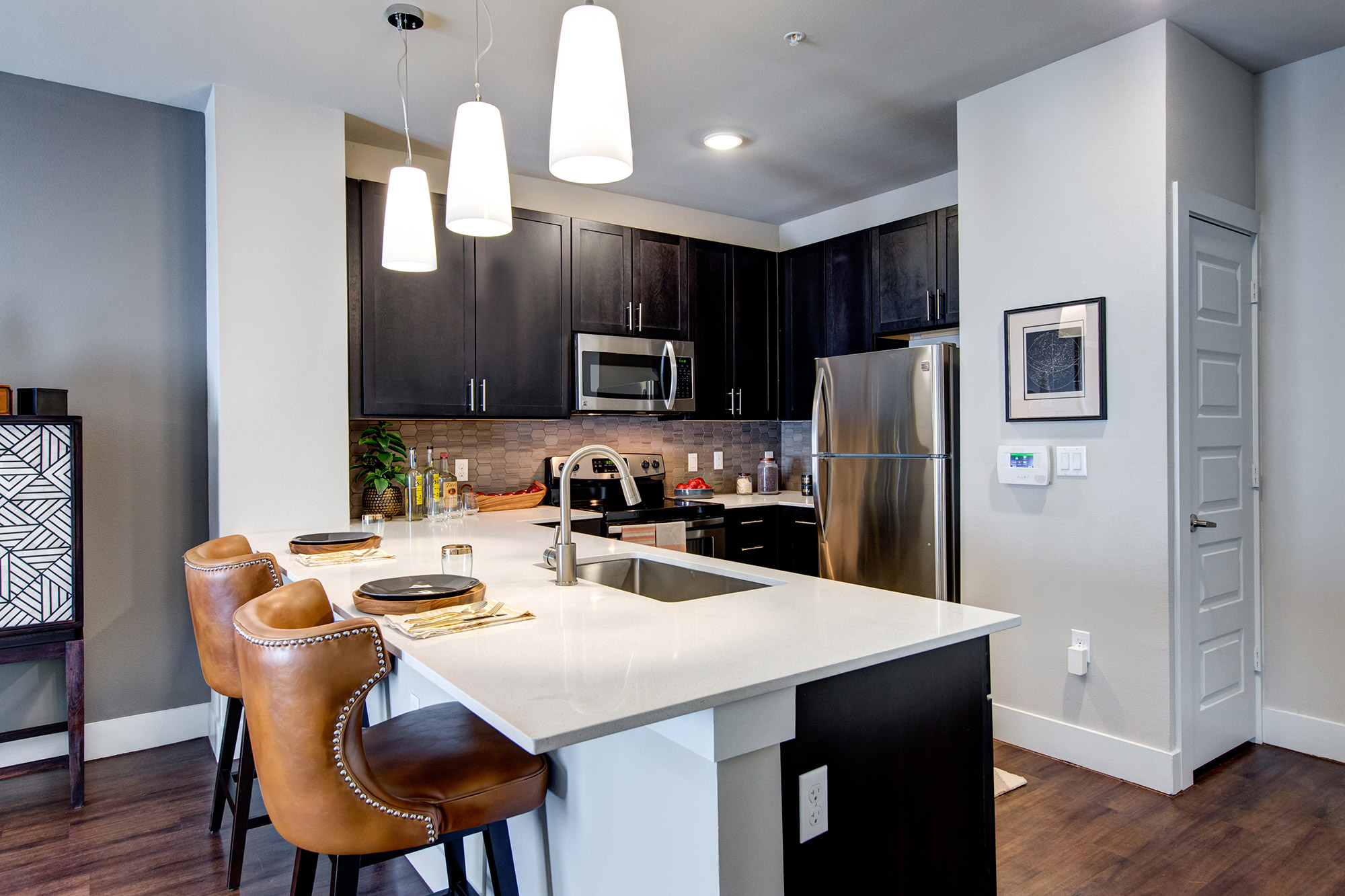 Kitchen with quartz counters and bar style seating, stainless steel appliances, pantry and designer lighting