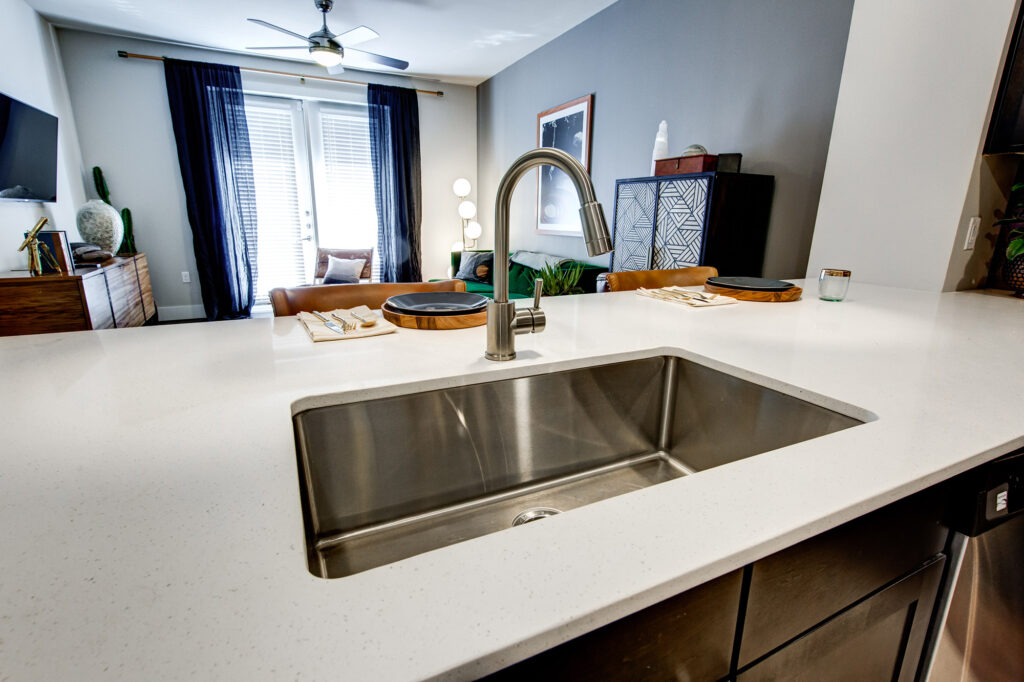 Large single basin stainless steel sink in kitchen with quartz counters