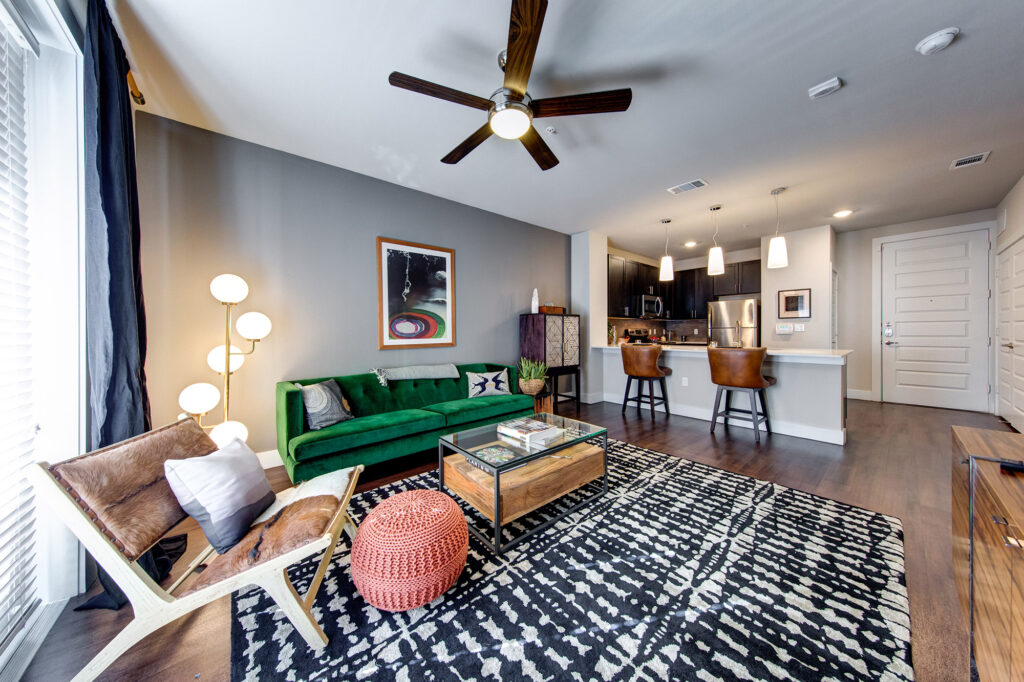 Open concept living room with ceiling fan, wood-style floors and door to patio that is open to the kitchen with stainless steel appliances